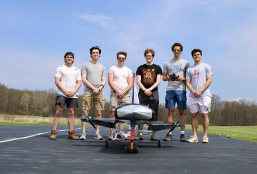2026 Design, Build, Fly team consisting of six male college students standing on the runway behind their finished aircraft
