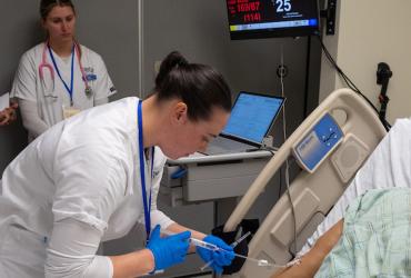A Kent State University nursing student administers IV medication to a manikin during a simulation while two classmates observe. (Photo credit: Bob Christy)