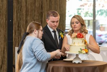 Brooklyn Fockler Leshon assists the bride and groom in staging the cutting of the wedding cake. 