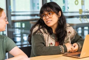 Two students talking at a table after class.