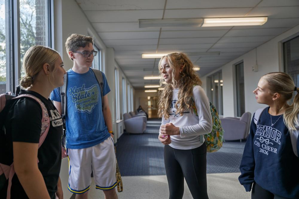 Four students with backpacks talk together in a campus hallway.
