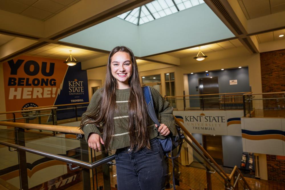 A student with a backpack smiles while standing in the atrium of a campus building.