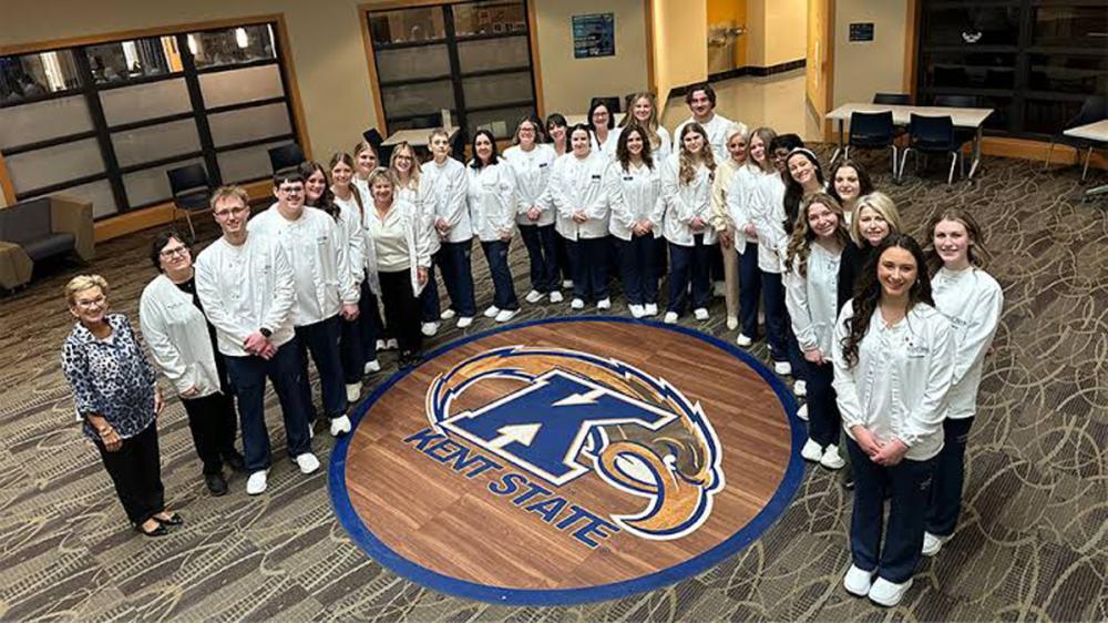 A group of nursing students and faculty stand together around a �Ը������� logo in a campus building.