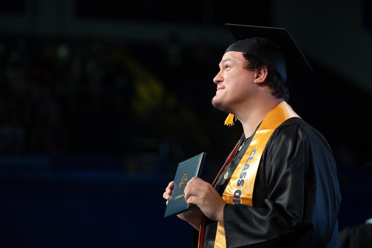 A new  graduate proudly holds his diploma during the summer 2024 commencement ceremony. (Photo credit: Bob Christy, )