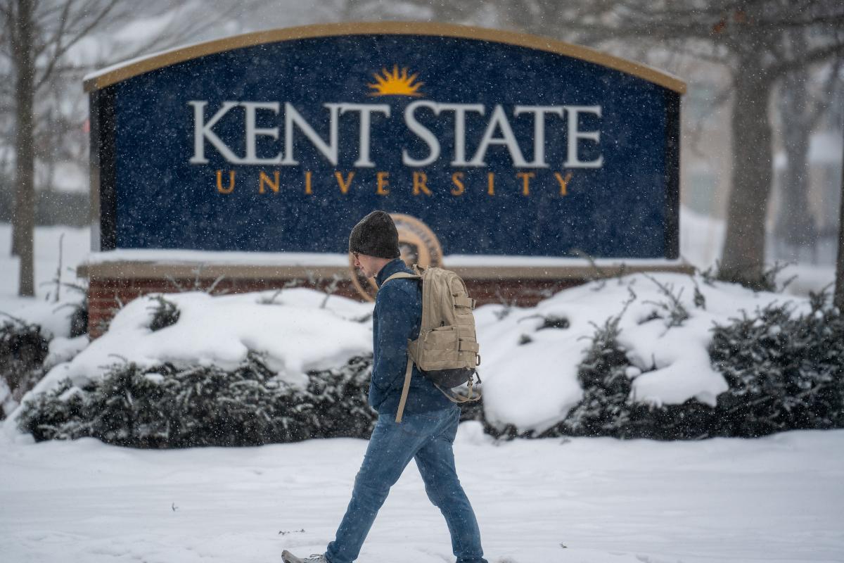 Person walking past the 5XÉçÇø sign during a snowfall, carrying a backpack.