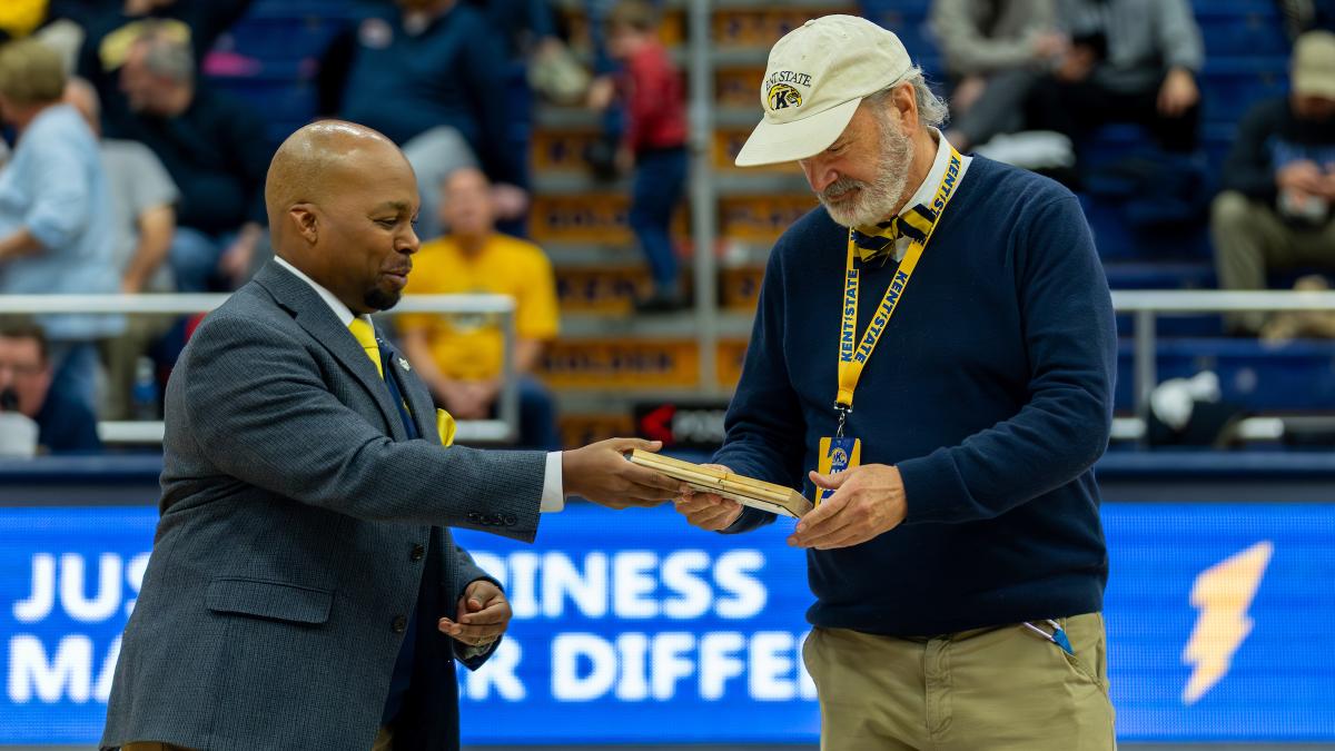 Two individuals at a sporting event, one wearing a "ɫҹ" sweater, exchanging documents in a basketball arena.