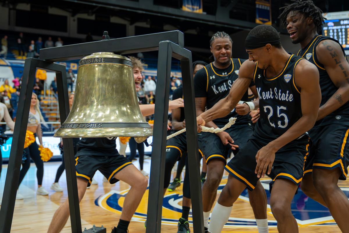 ɫҹ basketball players celebrating by ringing a large victory bell on the court.