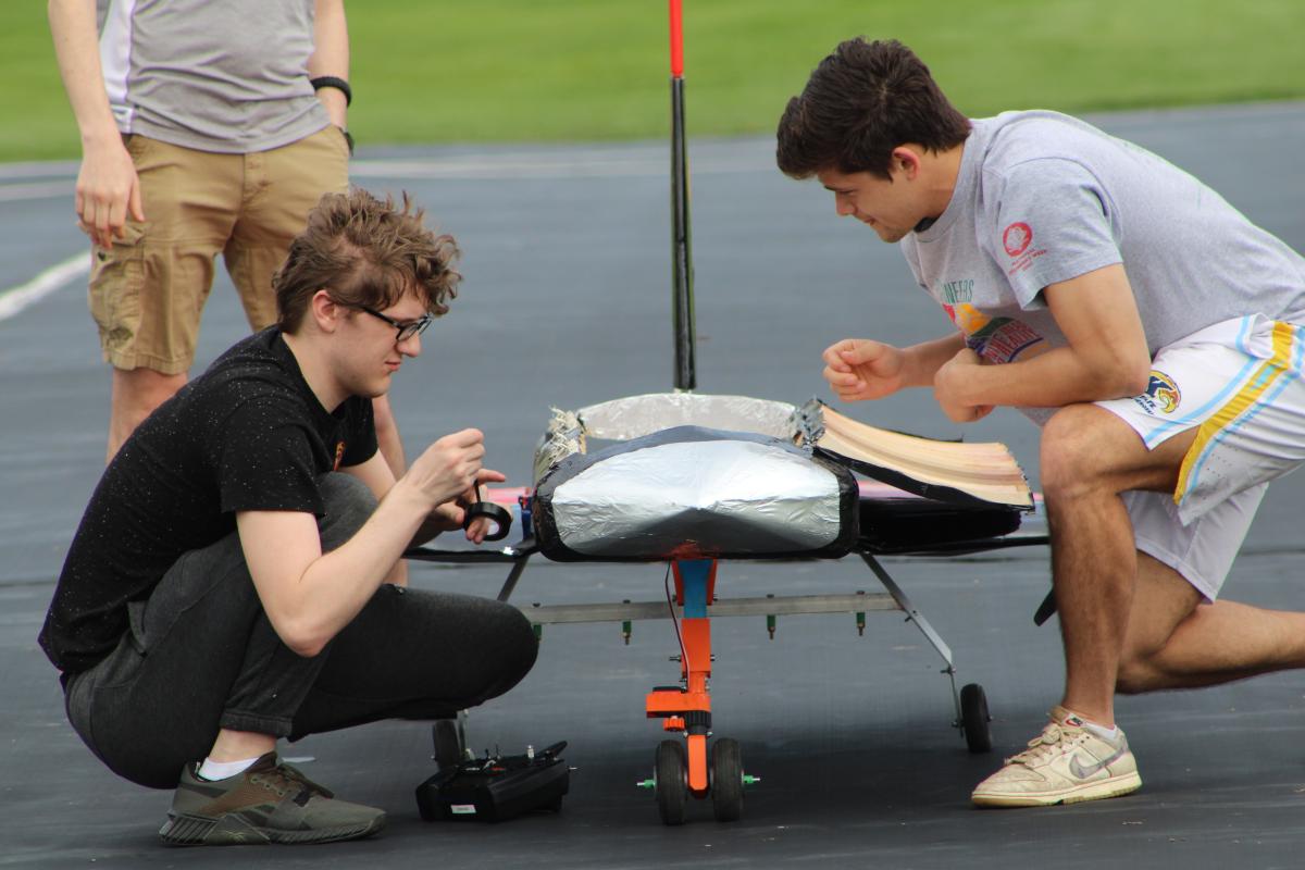 Two male students from Kent State's Design, Build, Fly team knell next to their aircraft to make adjustments.