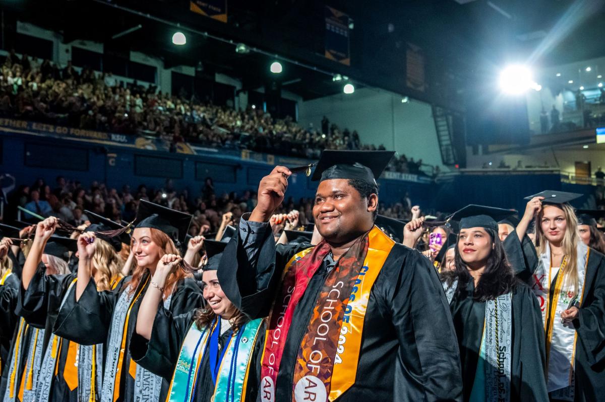 Several graduating students at commencement, dressed in their caps and gowns, getting ready to turn their tassels to signify graduation