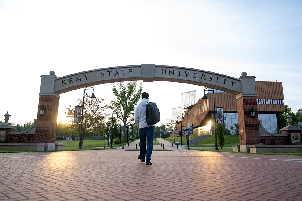 A student walks under the Kent State arch at sunrise.