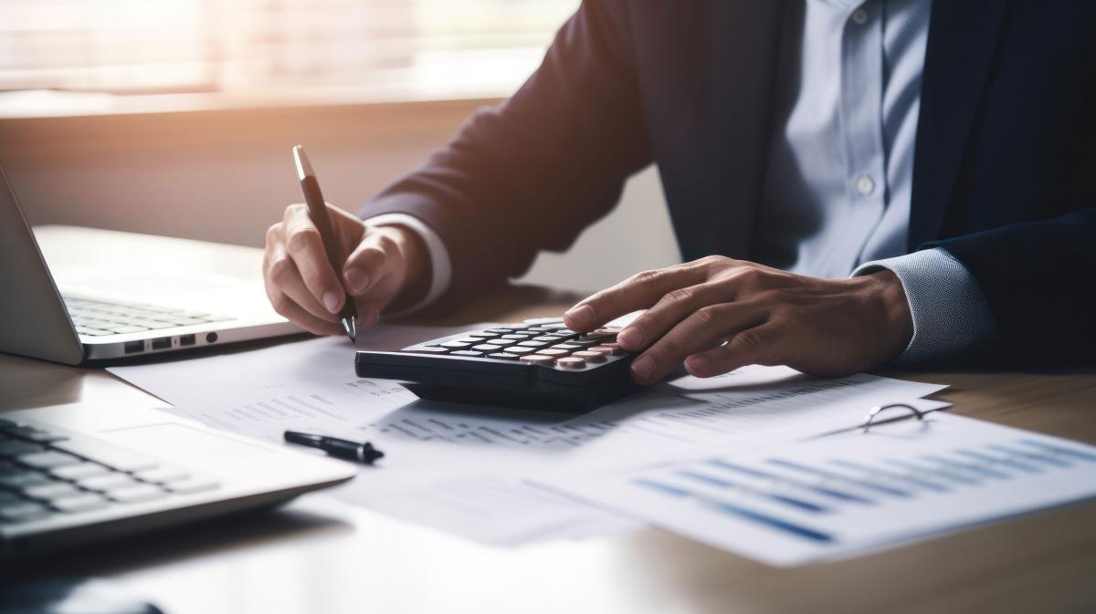 An accountant using a calculator and laptop and looking at tax forms.