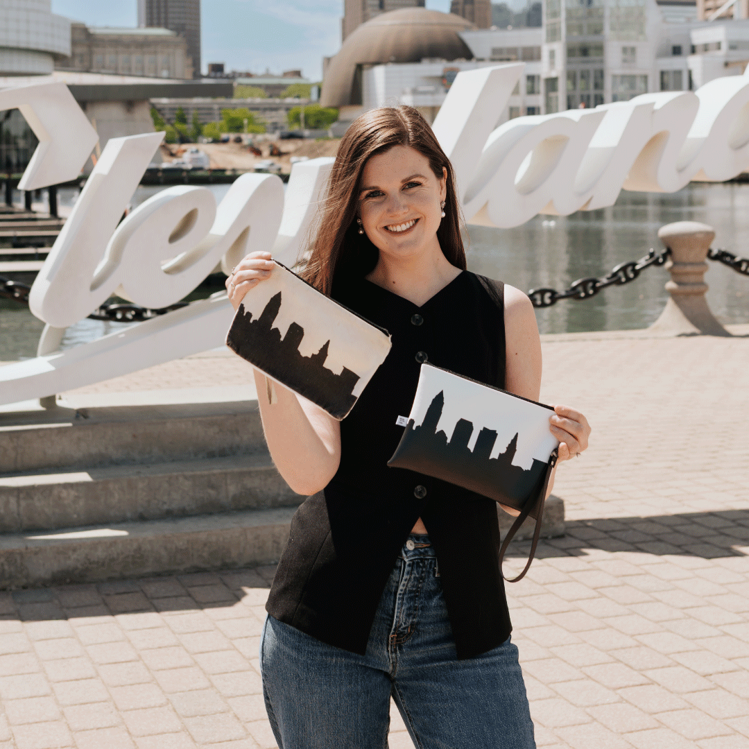 Anne Johnson poses in front of the cleveland sign on the lake while holding her custom handbags