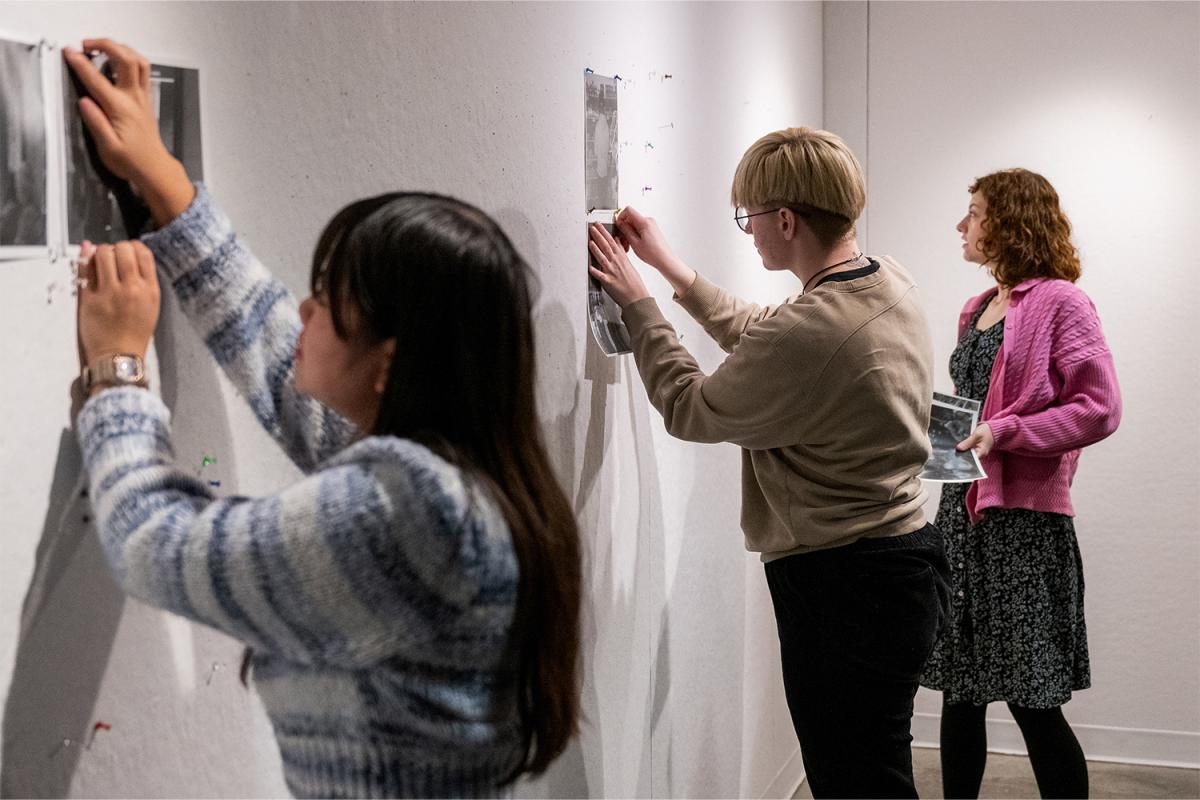 students hanging photos on wall for critique