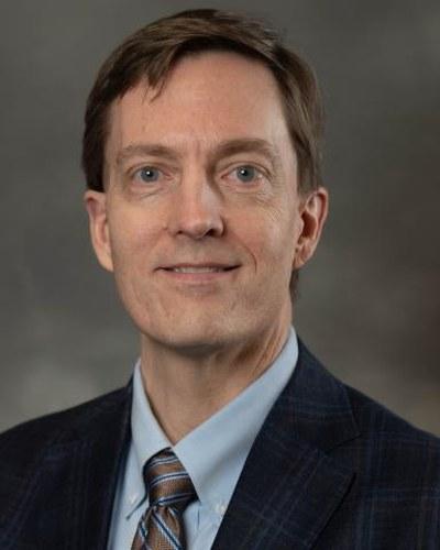 Professional portrait of a man in business attire, photographed against a neutral background.