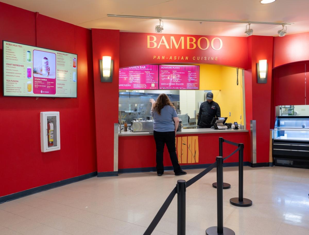 Exterior of Bamboo within the Student Center Hub. Mainly red walls with yellow accents, a walk-up counter for ordering, and menu screens