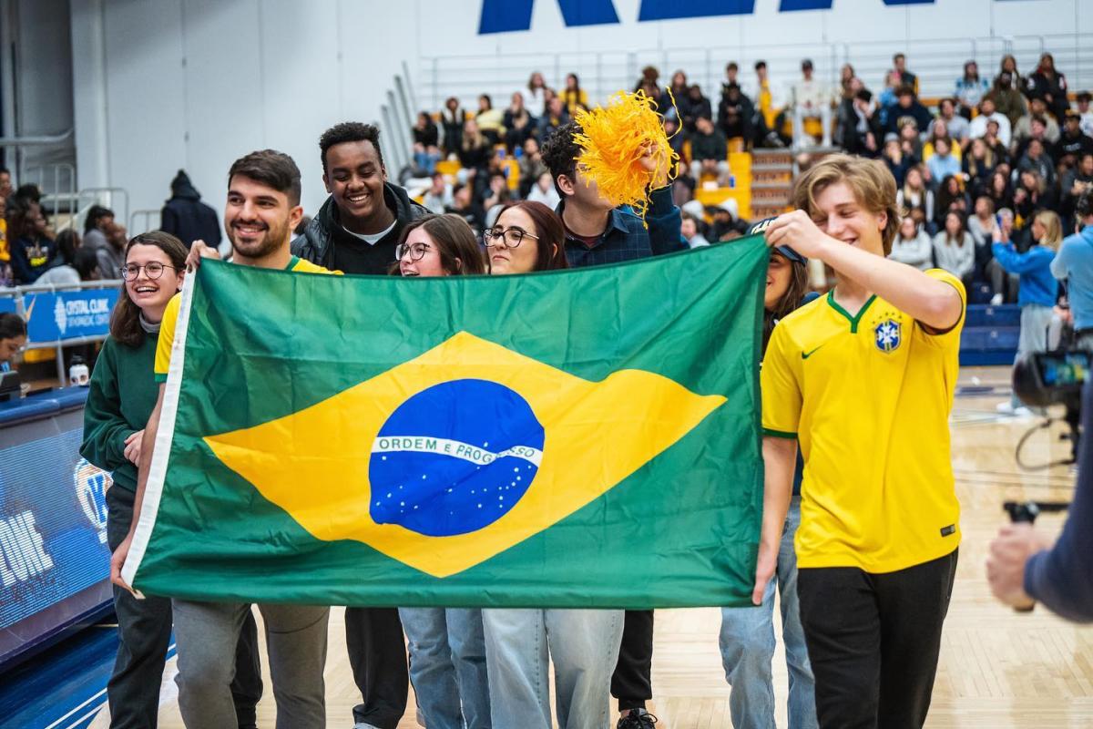 Gabriel and other students from Brazil holding up the Brazilian flag at a basketball game.