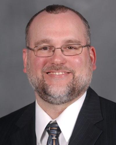 Formal portrait of a man in a suit smiling toward the camera with a studio background.