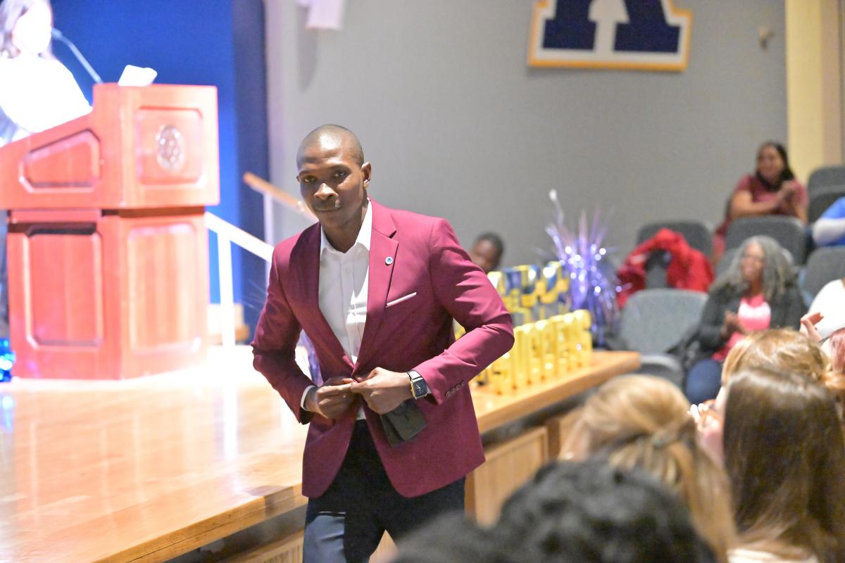 Person in a red blazer walking confidently towards the camera in a 鶹ѡauditorium during an event.