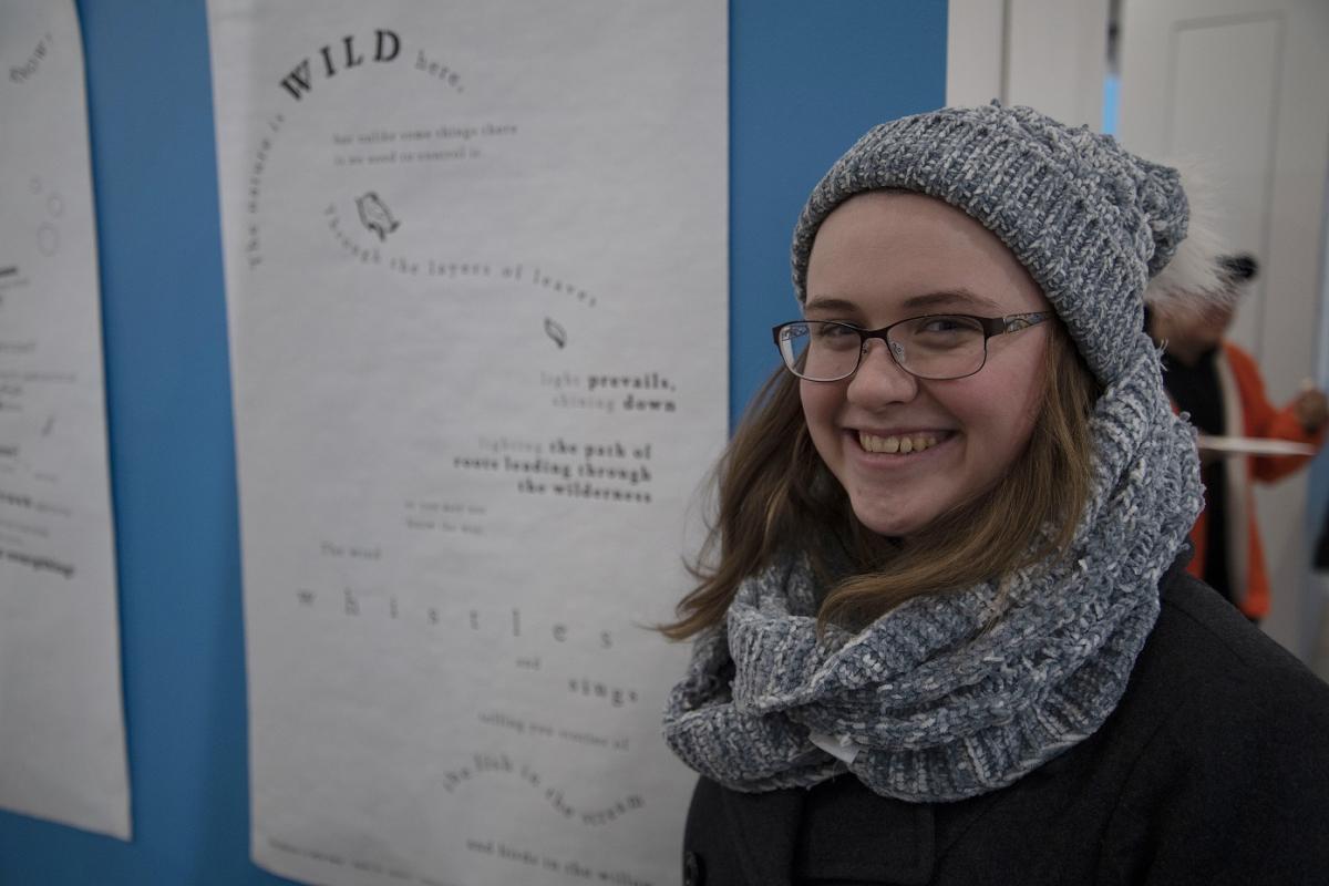 A VCD student stands next to her design at the Concrete Poetry Gallery Opening
