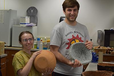 Anna Mika (left) and Dan Wilcox (right) show the difference between ceramic and soapstone pottery that they made in the lab.