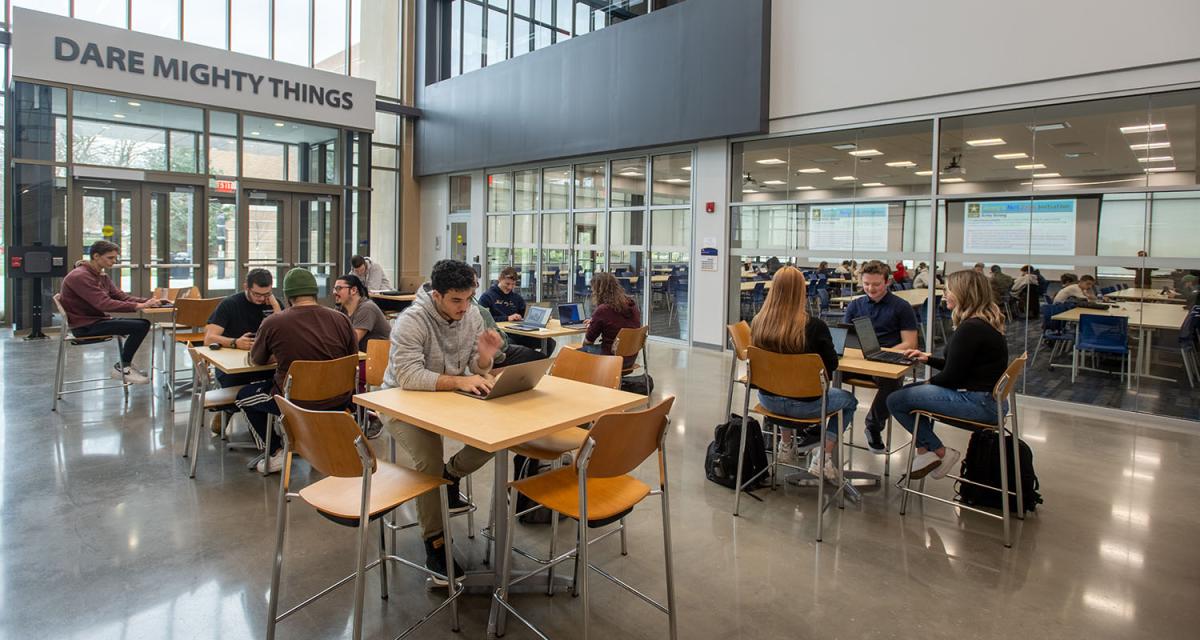 Inside the Aeronautics & Engineering building main atrium where several students are seated at raised tables.