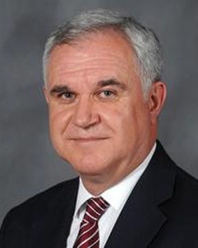Professional portrait of a man facing the camera against a studio backdrop.