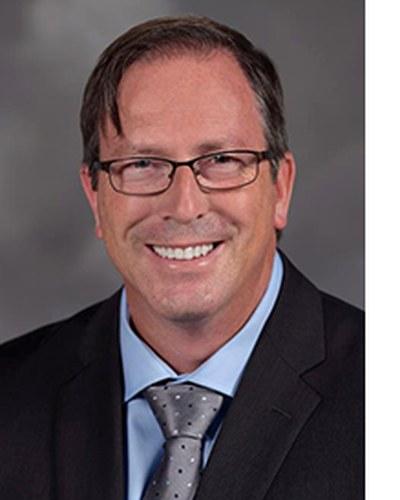Professional headshot of a man in business attire against a neutral background.