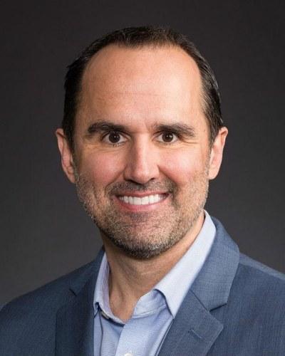 Professional portrait of a man in a suite with dark hair looking toward the camera with a simple background.