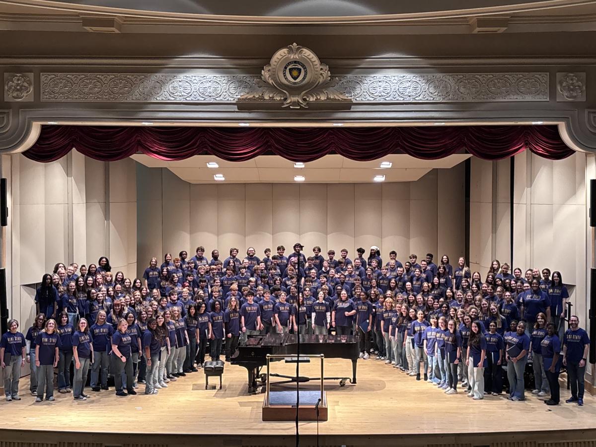 A crowd of music participants stand on-stage for a group photo, featuring around 100 people.