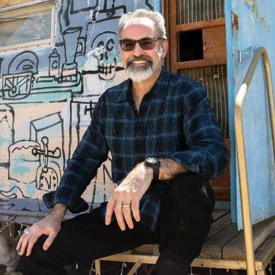 Iain Thomson sitting down in front of a colorful, outdoor background