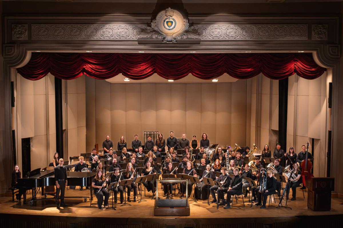 The wind ensemble posing on stage for a photo