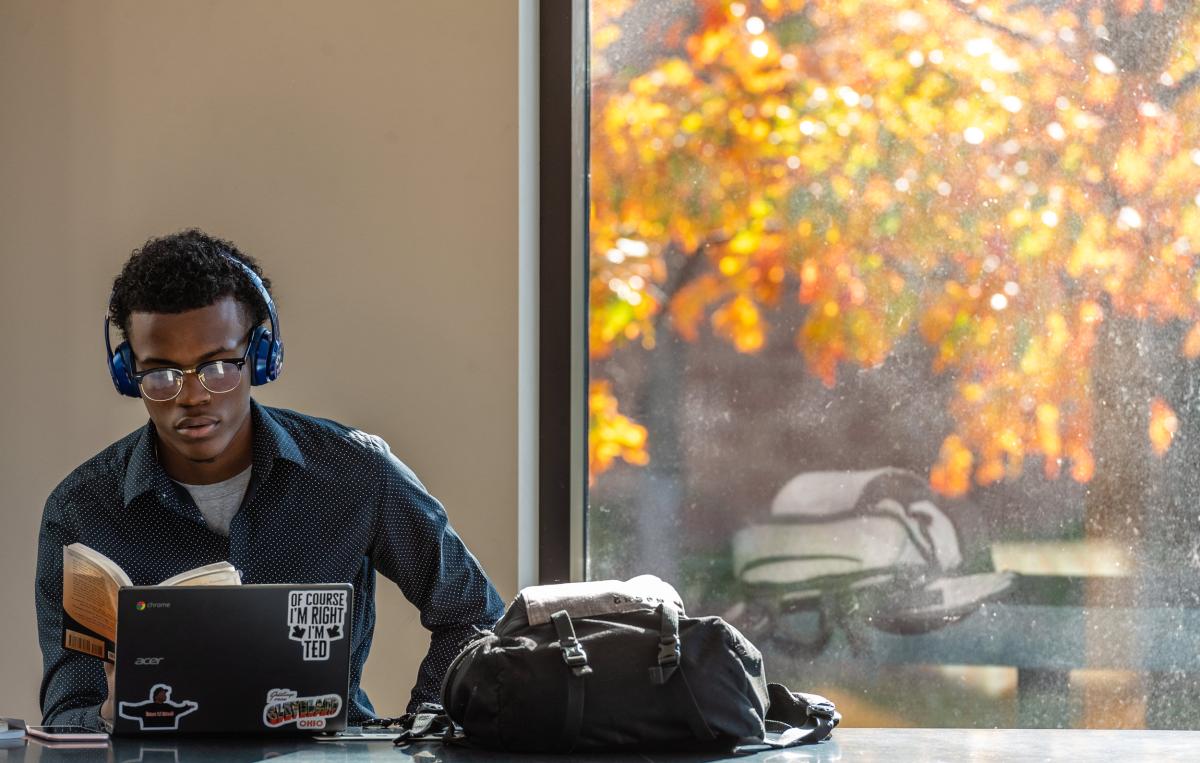 Kent State University student sits with his laptop and a book. (Photo credit: Rami Daud)