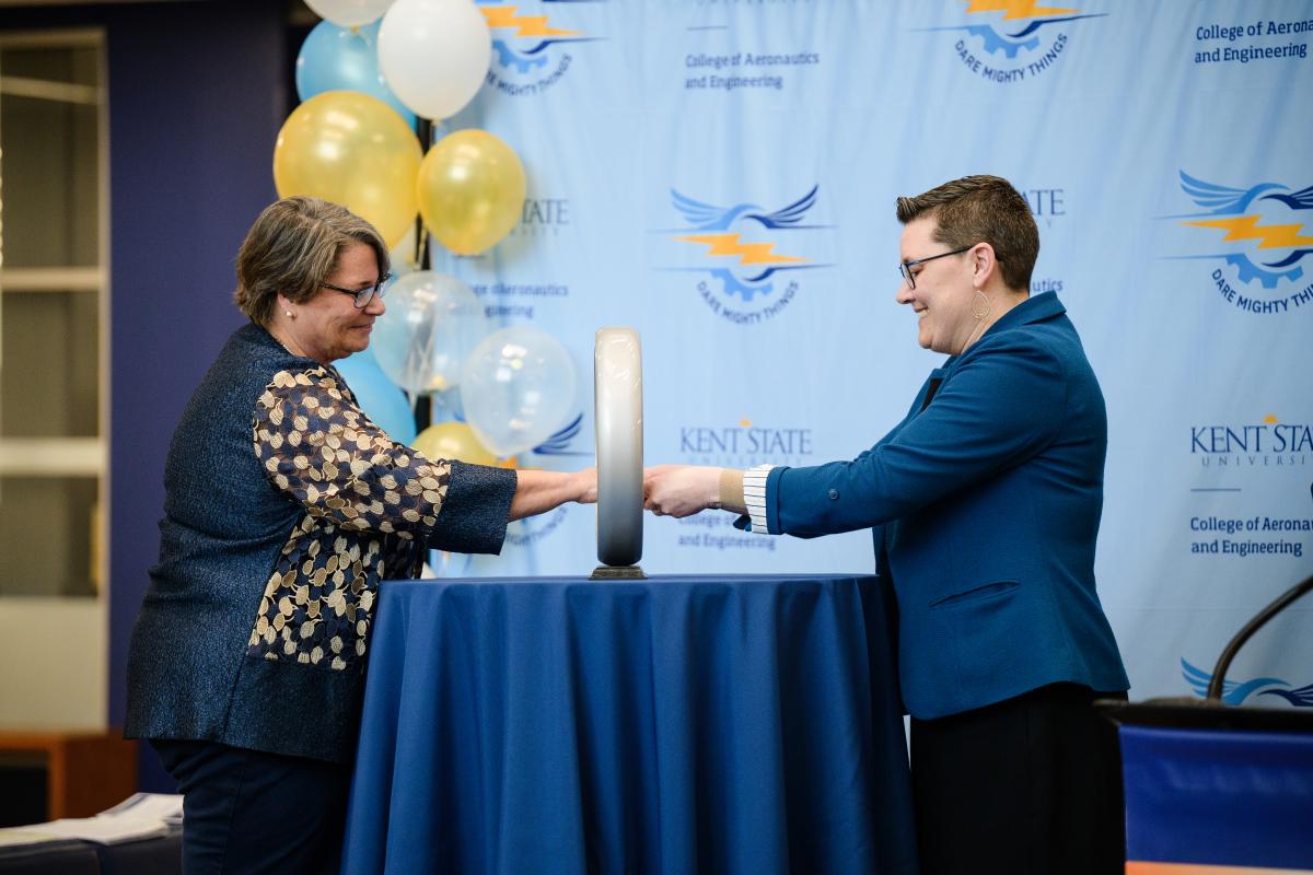 Two participants face each other across the Order of the Engineer ring sculpture, extending their right hands through the ceremonial ring as part of the induction ceremony tradition.