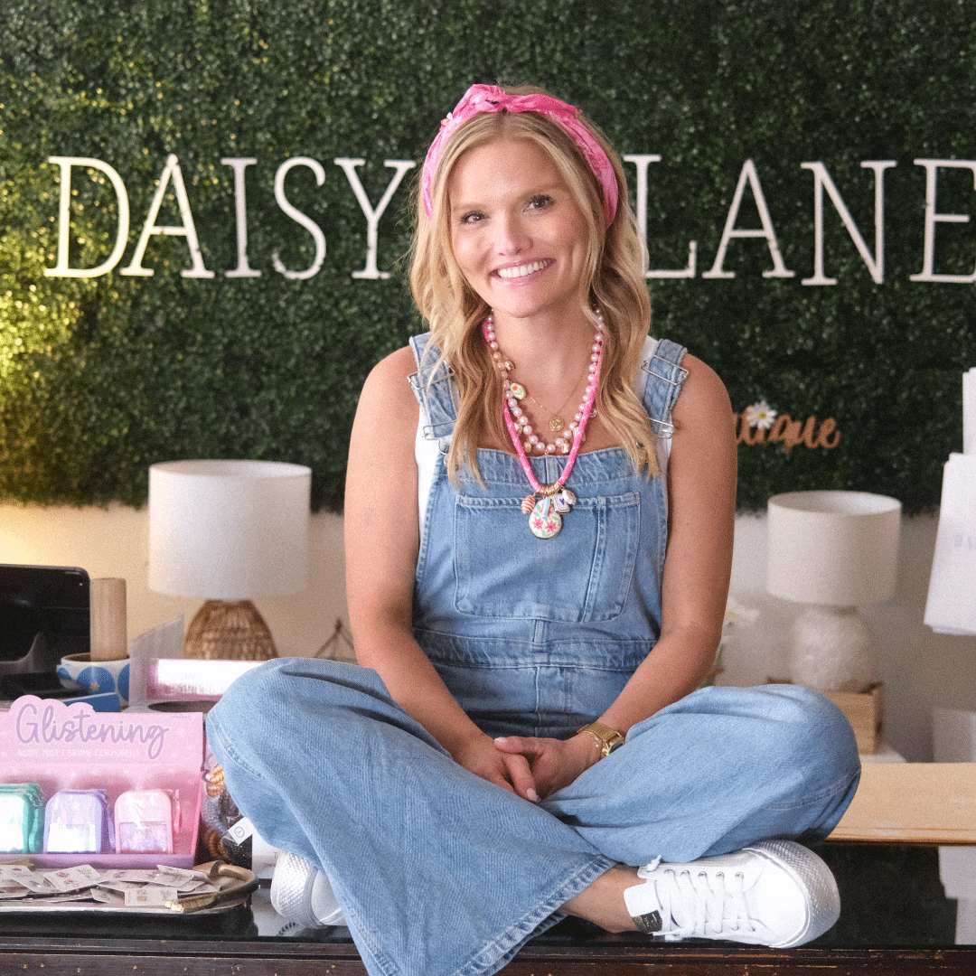 kylie gallagher sits cross-legged in denim overalls and a pink headband.