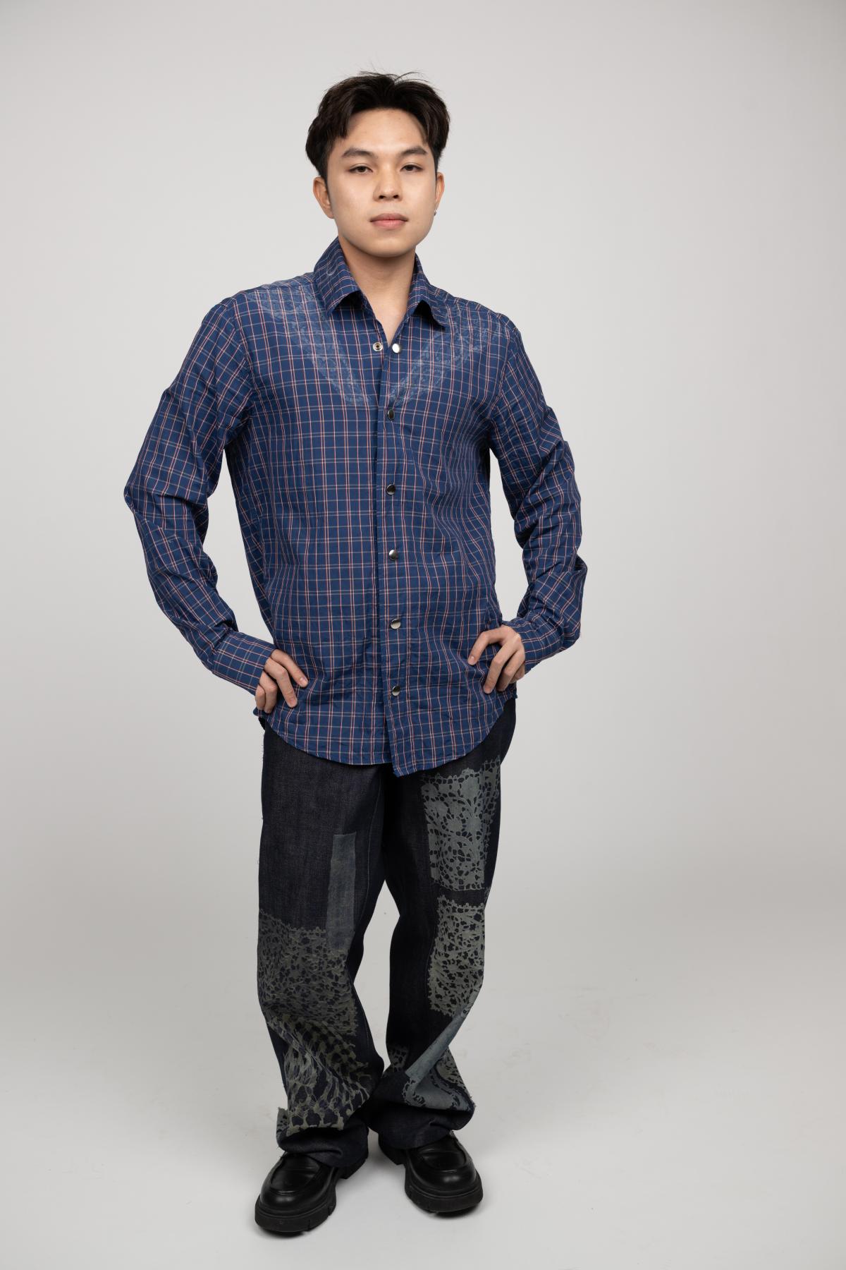 A model wear a plaid button up and black straight-legged jeans with patchwork features