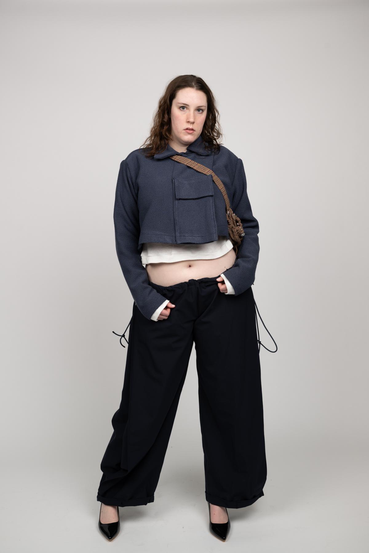 A model wears a denim jacket with a large pocket on the front, pair with a crossbody bag and wide-legged pants