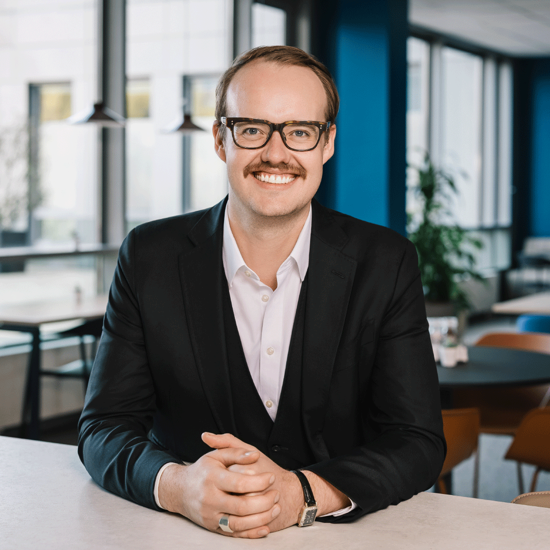Mason Henry Howell poses for a professional headshot, wearing a navy suit and white button up.  