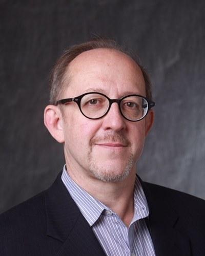 Headshot of a man in professional attire against a studio-style backdrop.