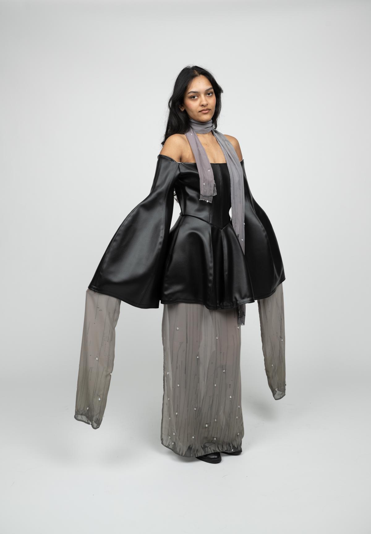 a model wears a formal gown made of leather, with a beaded sheer fabric under skirt and long off-the-shoulder bell sleeves