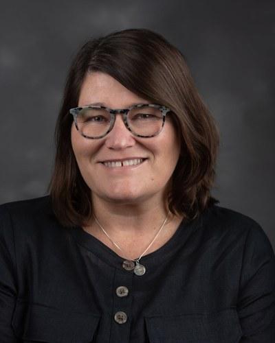 Head-and-shoulders professional headshot of a woman with a studio background.