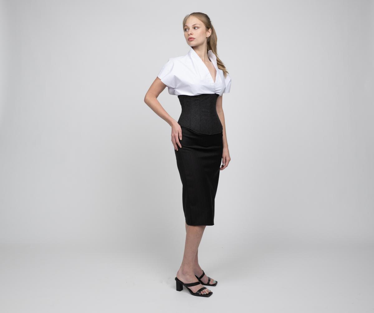 a model wears a short-sleeved white button up and long black pencil skirt with a black corset over top