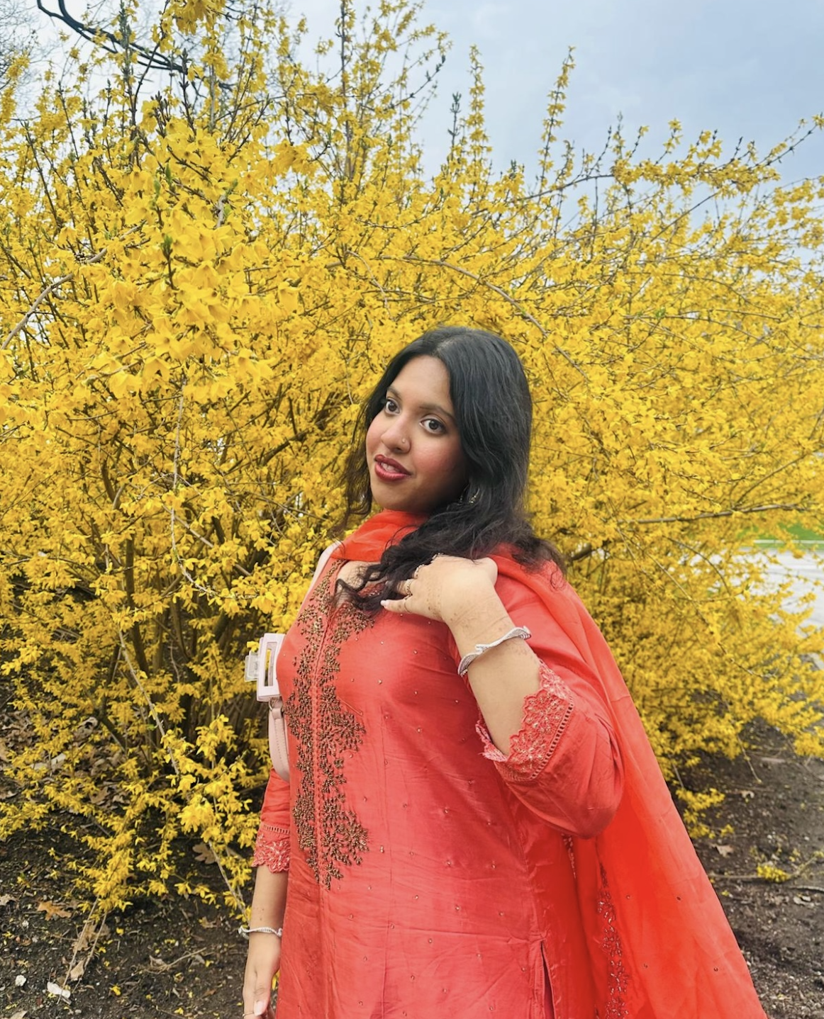 Ittiba in a red dress next to a yellow flowering bush.