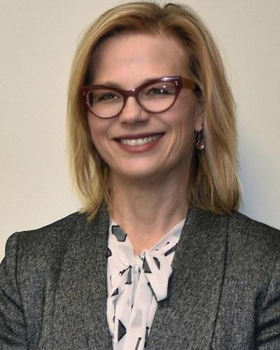 Professional portrait of a woman smiling toward the camera against a neutral background.