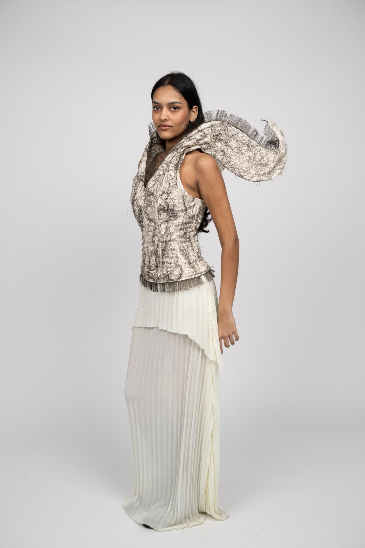 A model wears a white gown with tiered pleated fabric for the skirt and a structured corset with straps that seem to form into wings.