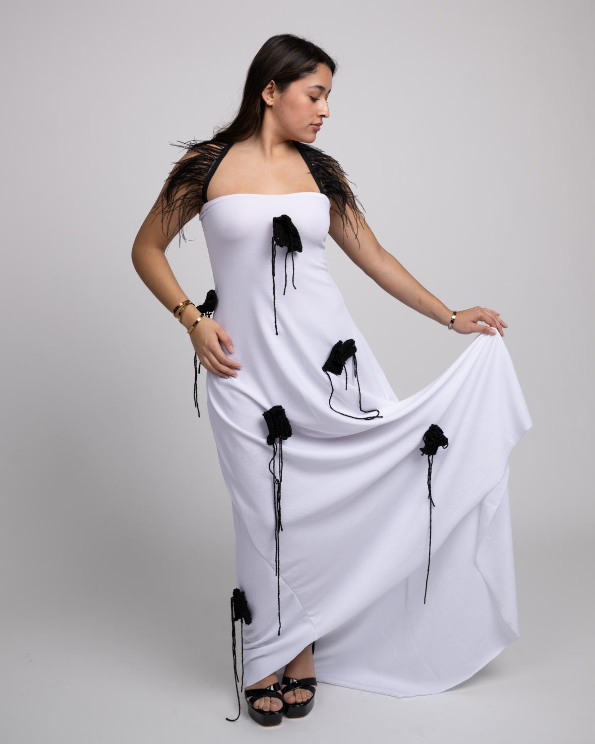 a models wears a white gown with black, knit appliques and feather straps