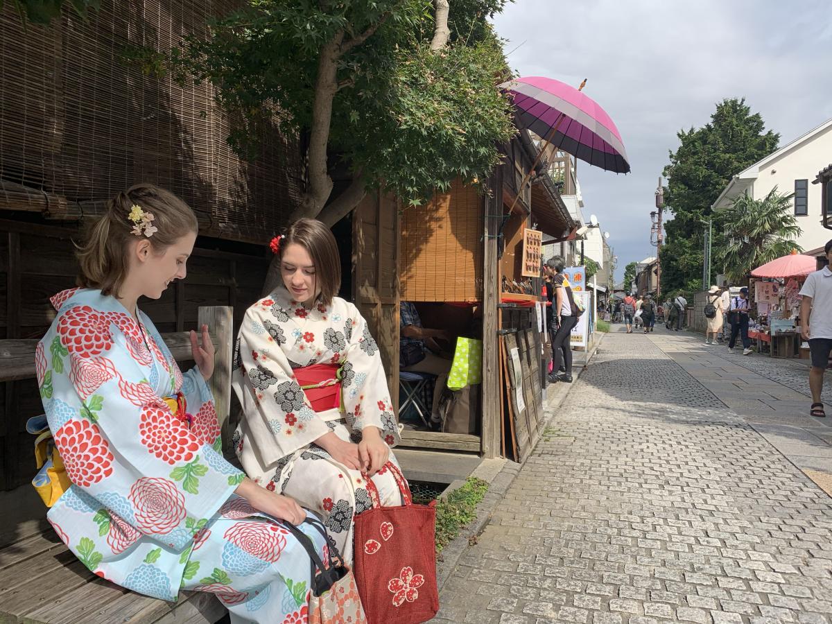 Two students in kimonos sitting on a bench in Japan.