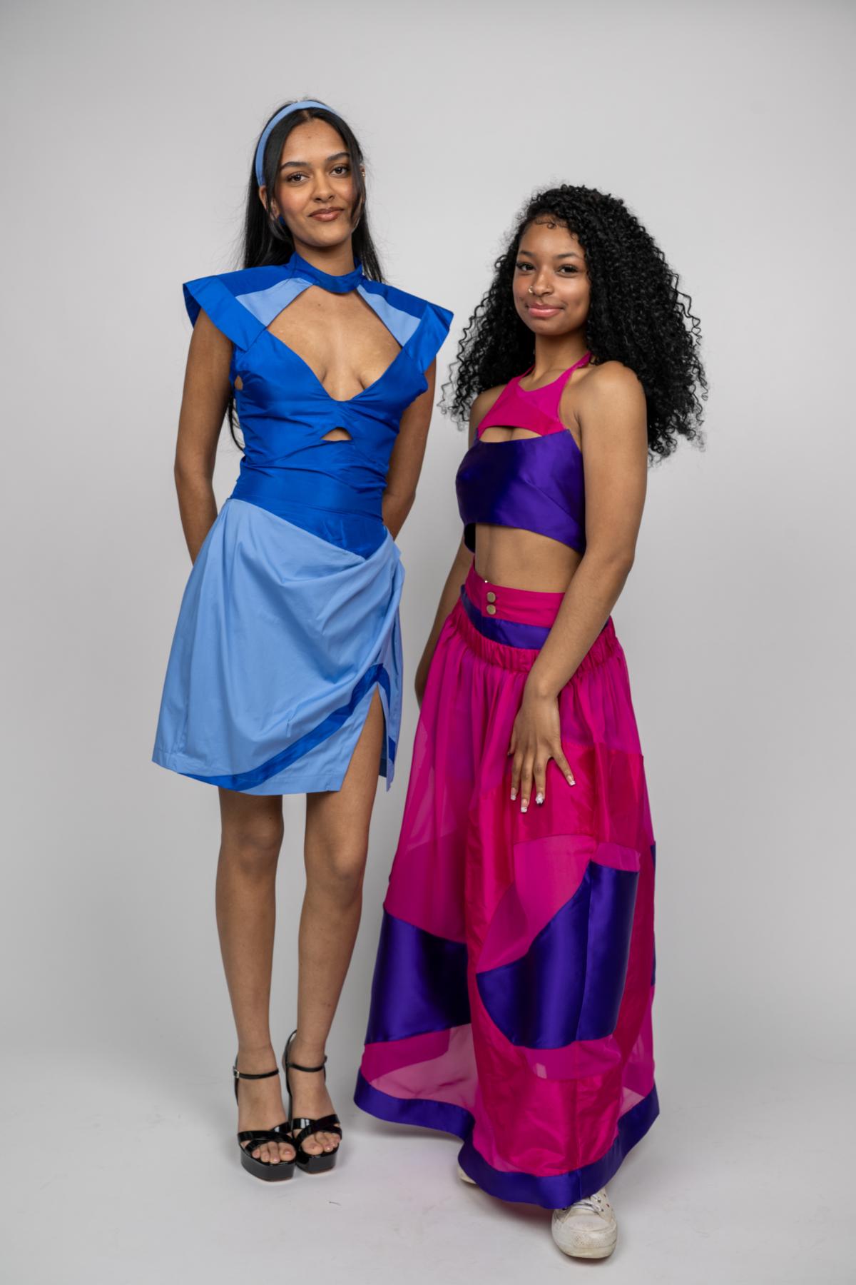 two models pose in retro inspired outfits. one wears a blue corseted mini dress with a cut our shape over the chest. the otherr wears a pink and purple two piece set