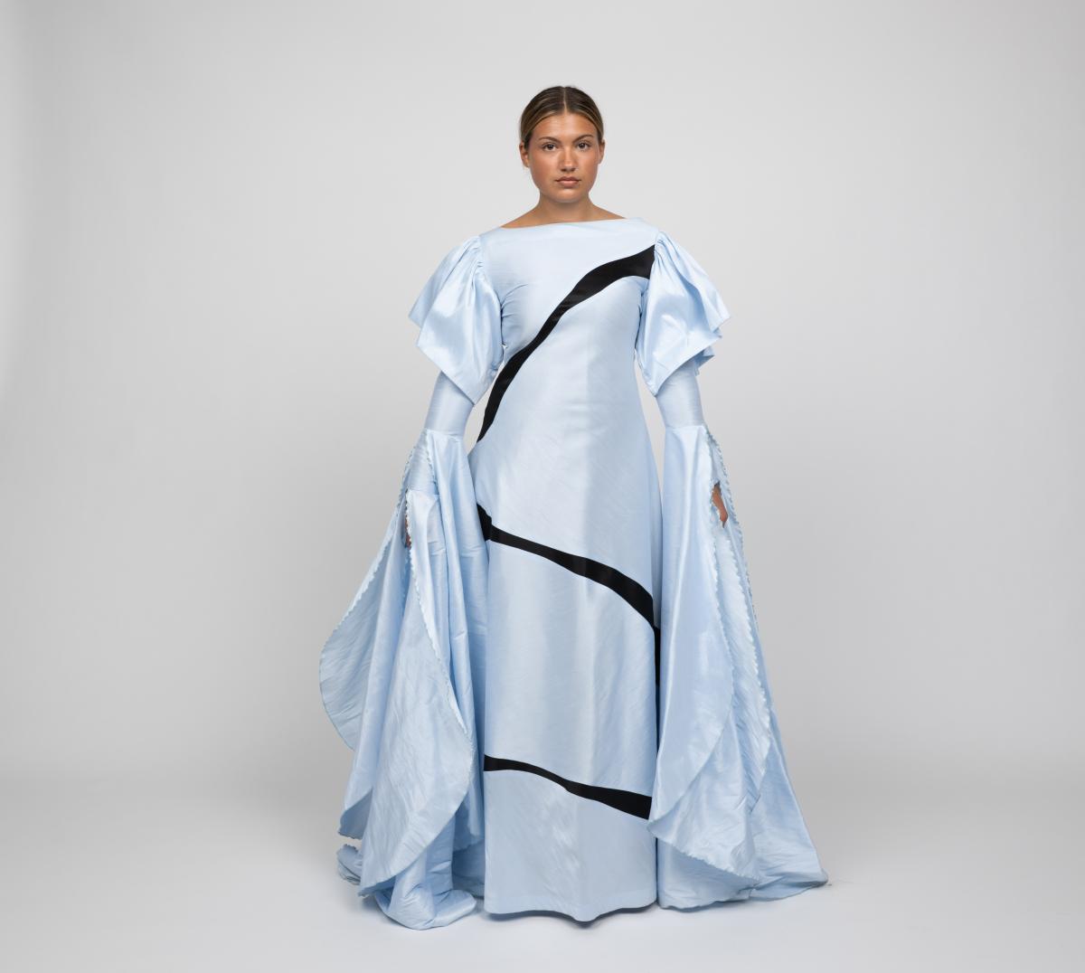 a model wears a floorlength light blue gown with extra-long bell sleeves and a black line wrapping around the garment