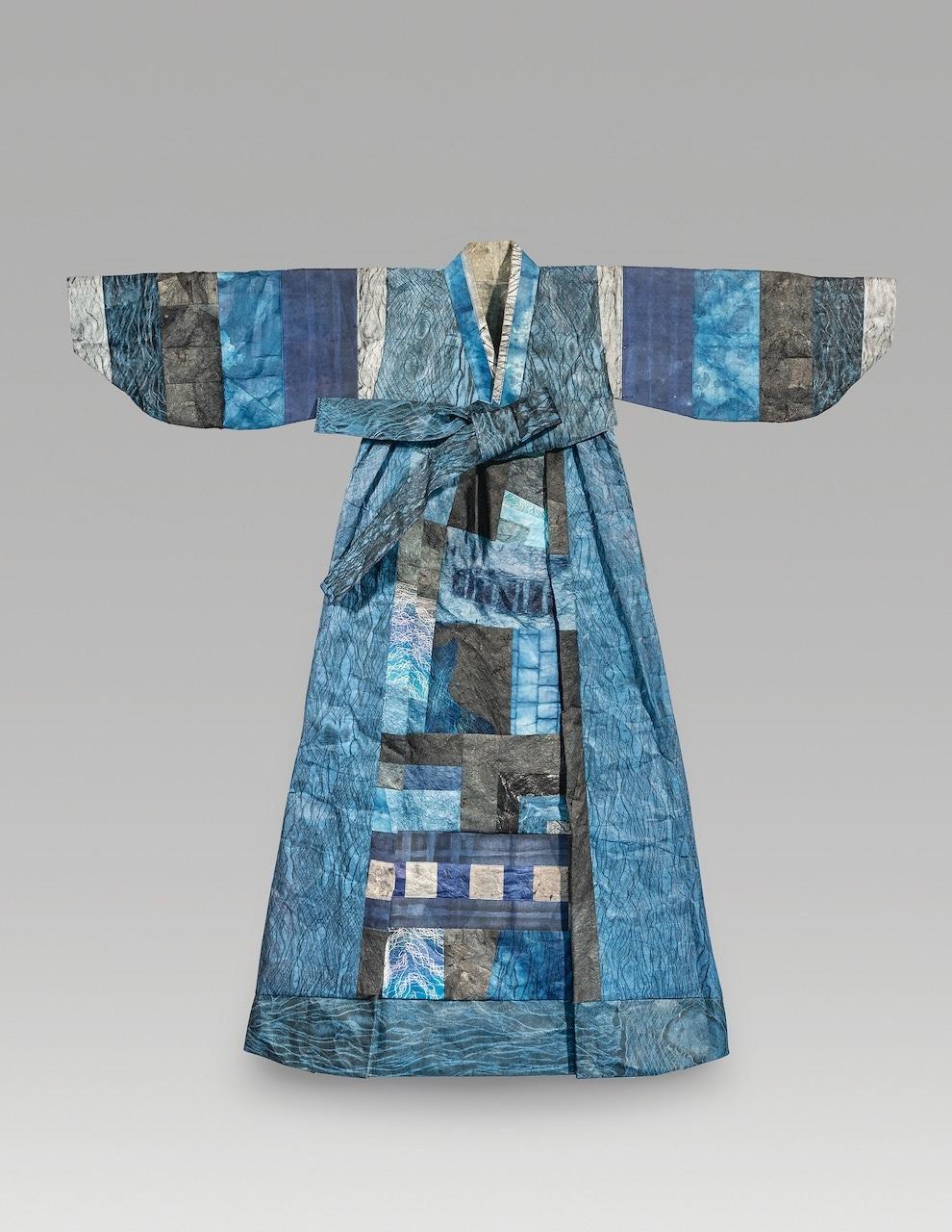 Dress with arms out to the sides; multiple colors and patterns consisting of blues, whites, dark colors.