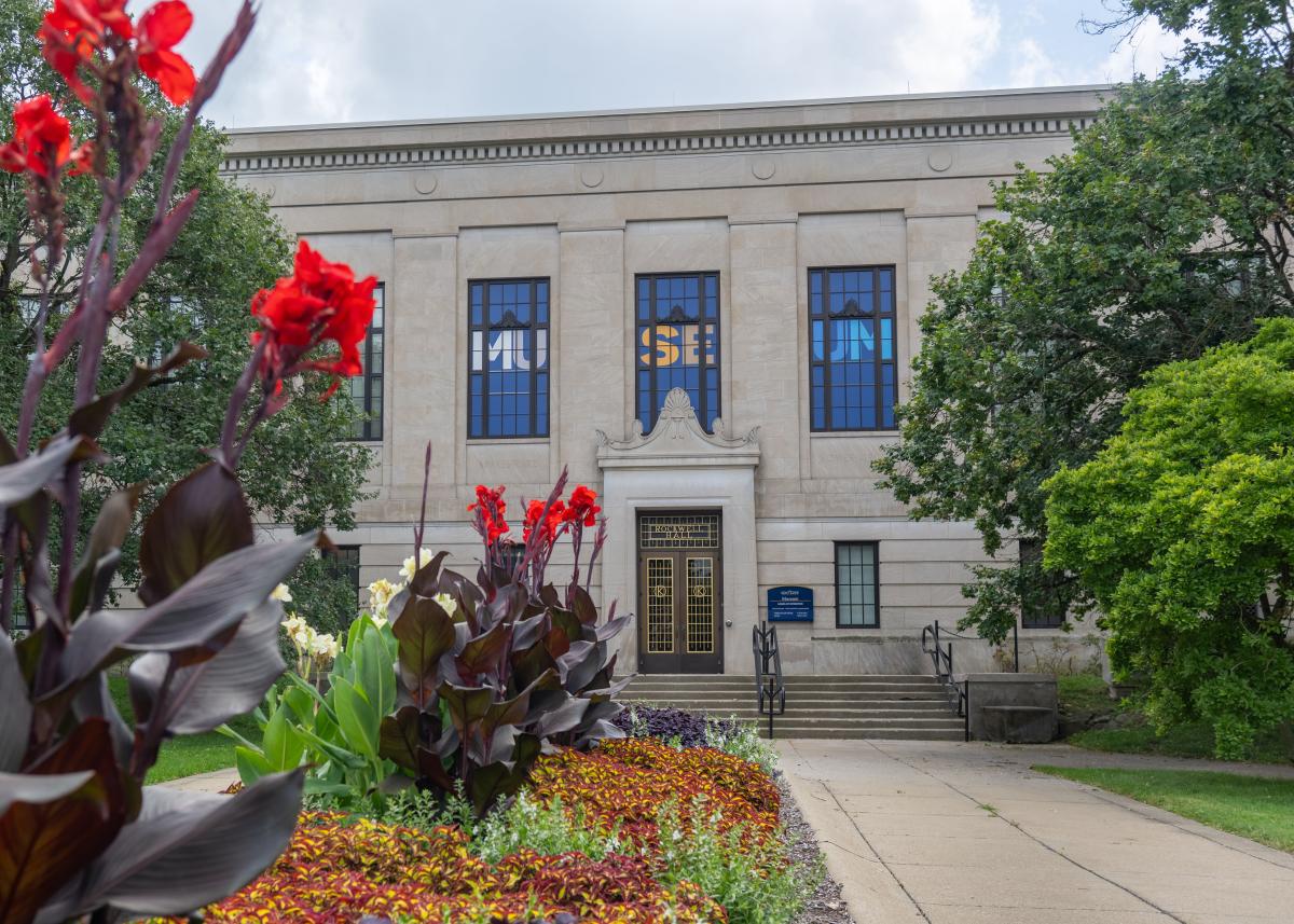 Light beige building with "Museum" showcased on its front and red flowers framing the image
